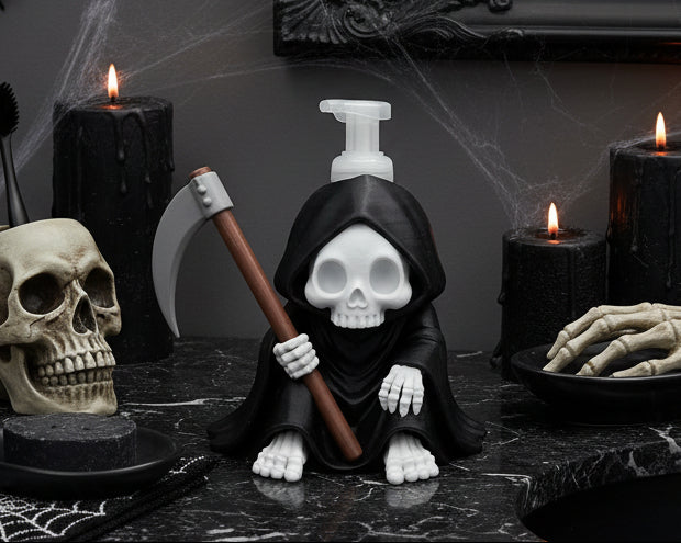 A Grim Reaper-shaped pump dispenser featuring a white skull face, black hooded body, white skeletal hands and feet, and a brown scythe prop, photographed against a white studio backdrop.